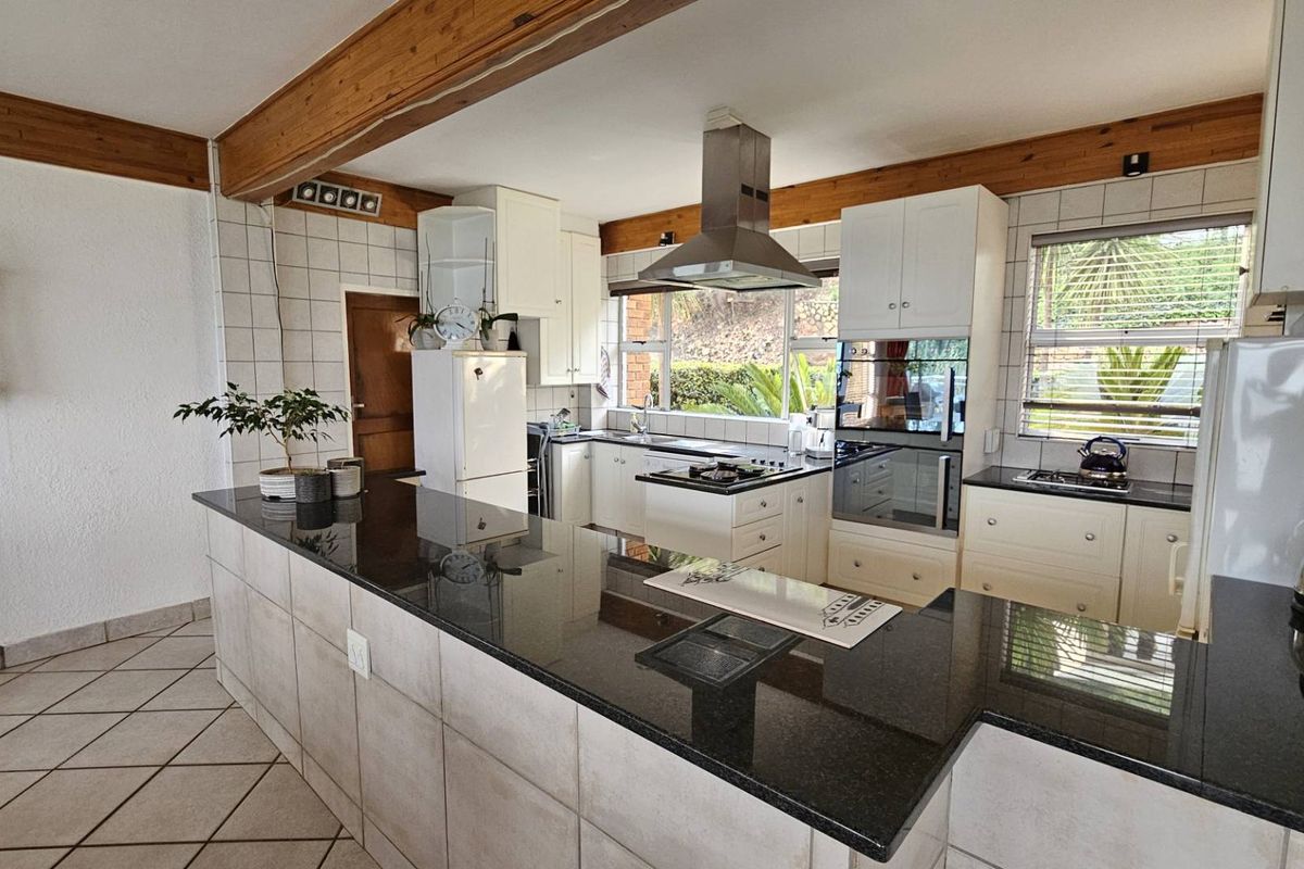 Spacious kitchen featuring a large granite breakfast bar, built-in oven, extractor fan, and ample cabinetry with a functional layout.