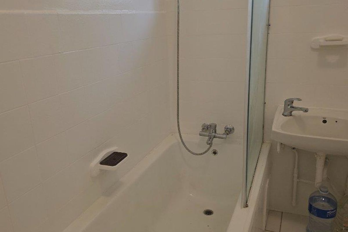 A functional bathroom featuring a bathtub with a shower mixer, glass screen, and a pedestal basin with tiled finishes throughout.