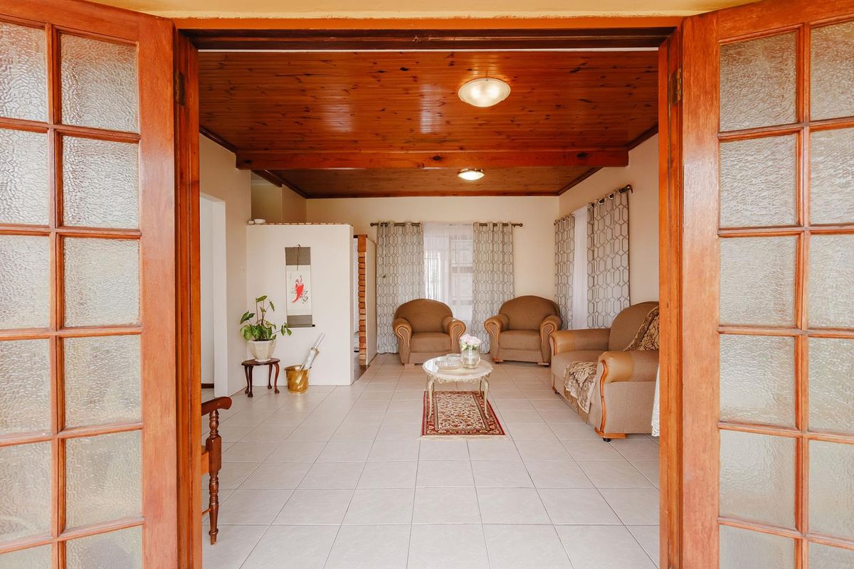 A living room featuring a warm timber-paneled ceiling, neutral tiled flooring, and double glass panel doors providing access to the space.