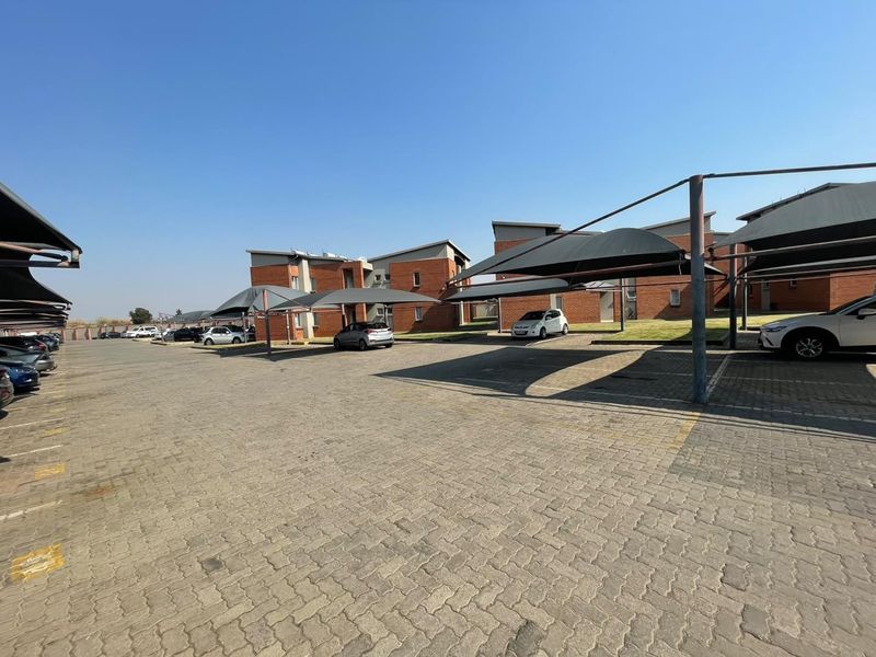 Exterior view of an apartment complex featuring a large paved parking area with dedicated shade cloth carports and brick building facades.