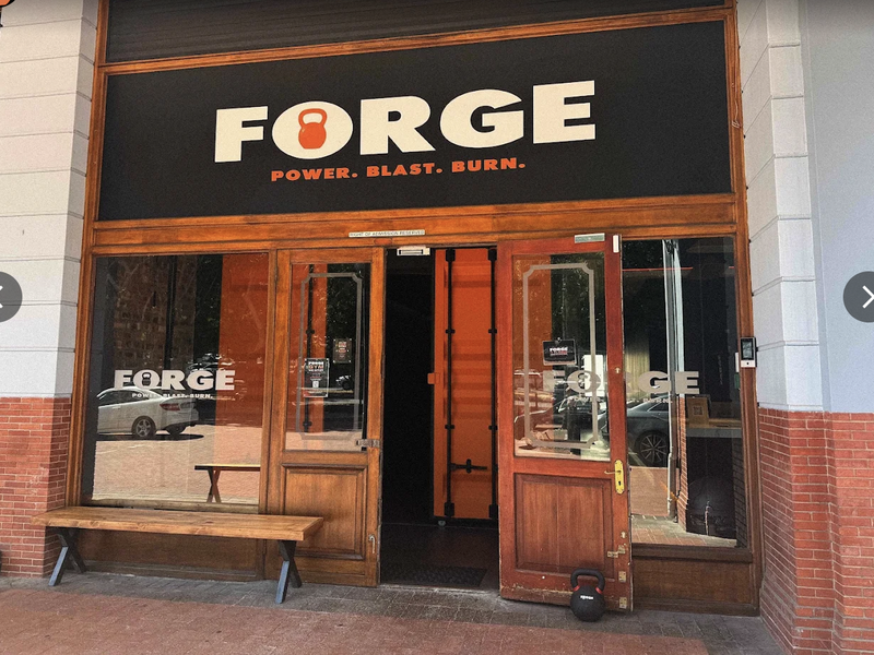 Front entrance of a retail gym space featuring a timber-framed glass door, brick facade, and prominent signage.