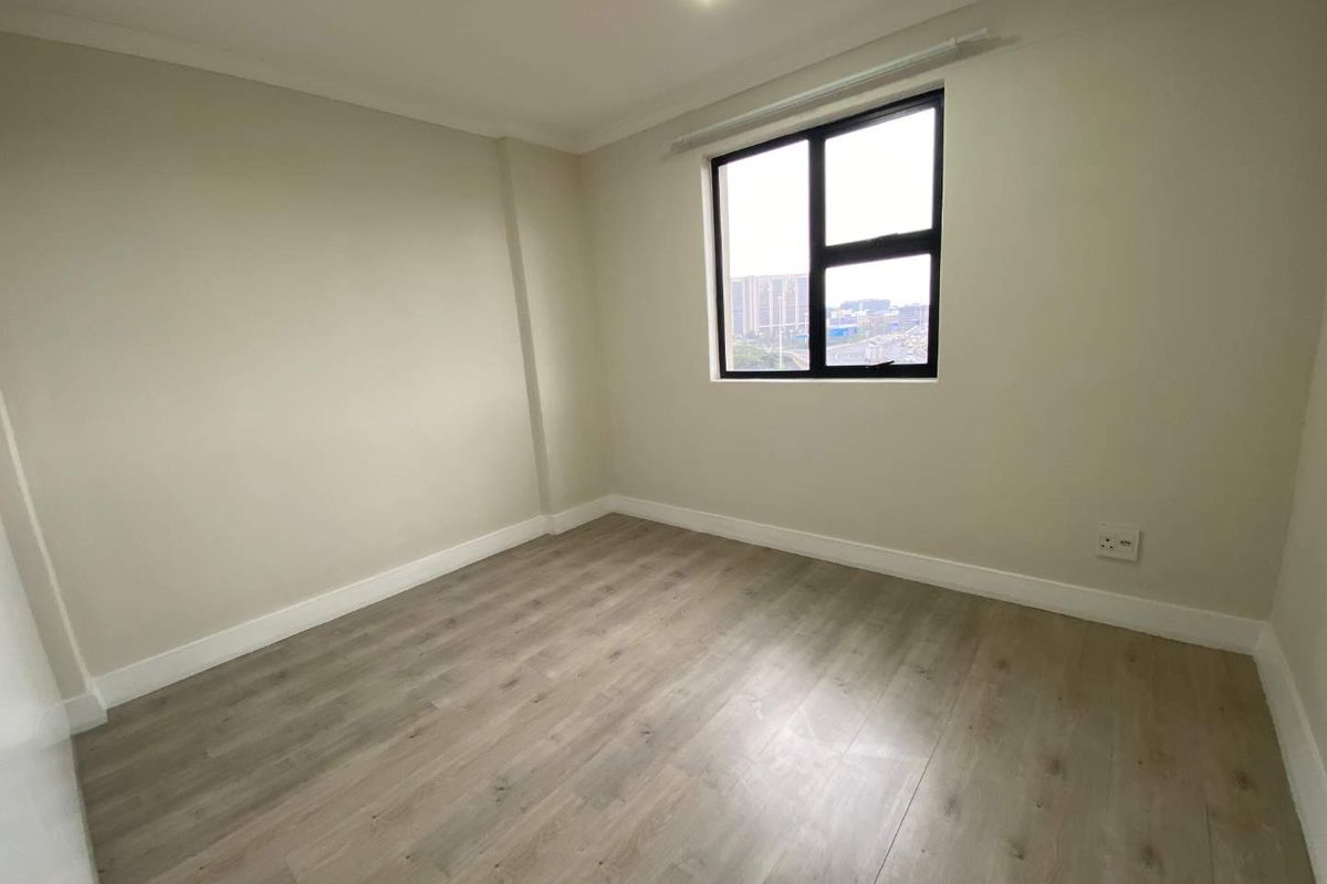 A bright, empty bedroom featuring modern wood-look laminate flooring, neutral wall finishes, and a window providing natural light.