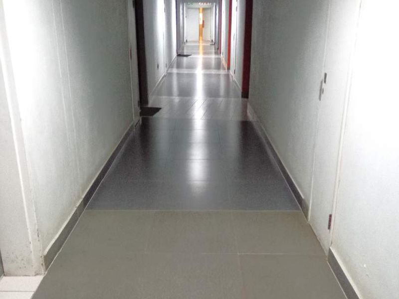 A long, well-lit residential hallway featuring neutral tiled flooring and multiple access doors along the corridor.