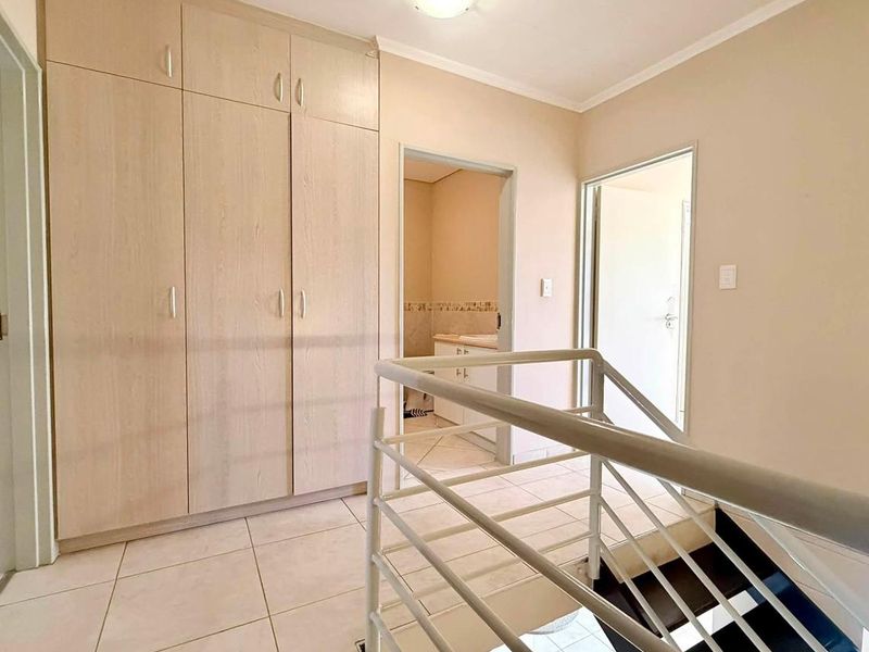 A bright upstairs hallway featuring built-in cupboards, tiled flooring, and a metal staircase railing, providing access to adjacent rooms.