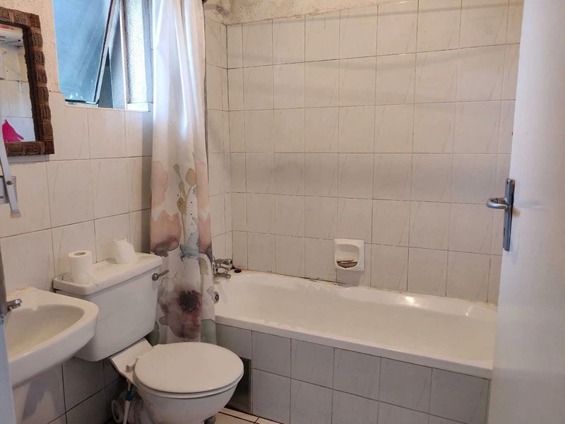 A dated bathroom featuring a standard bathtub, pedestal sink, and toilet with full-height wall tiling and an awning window.