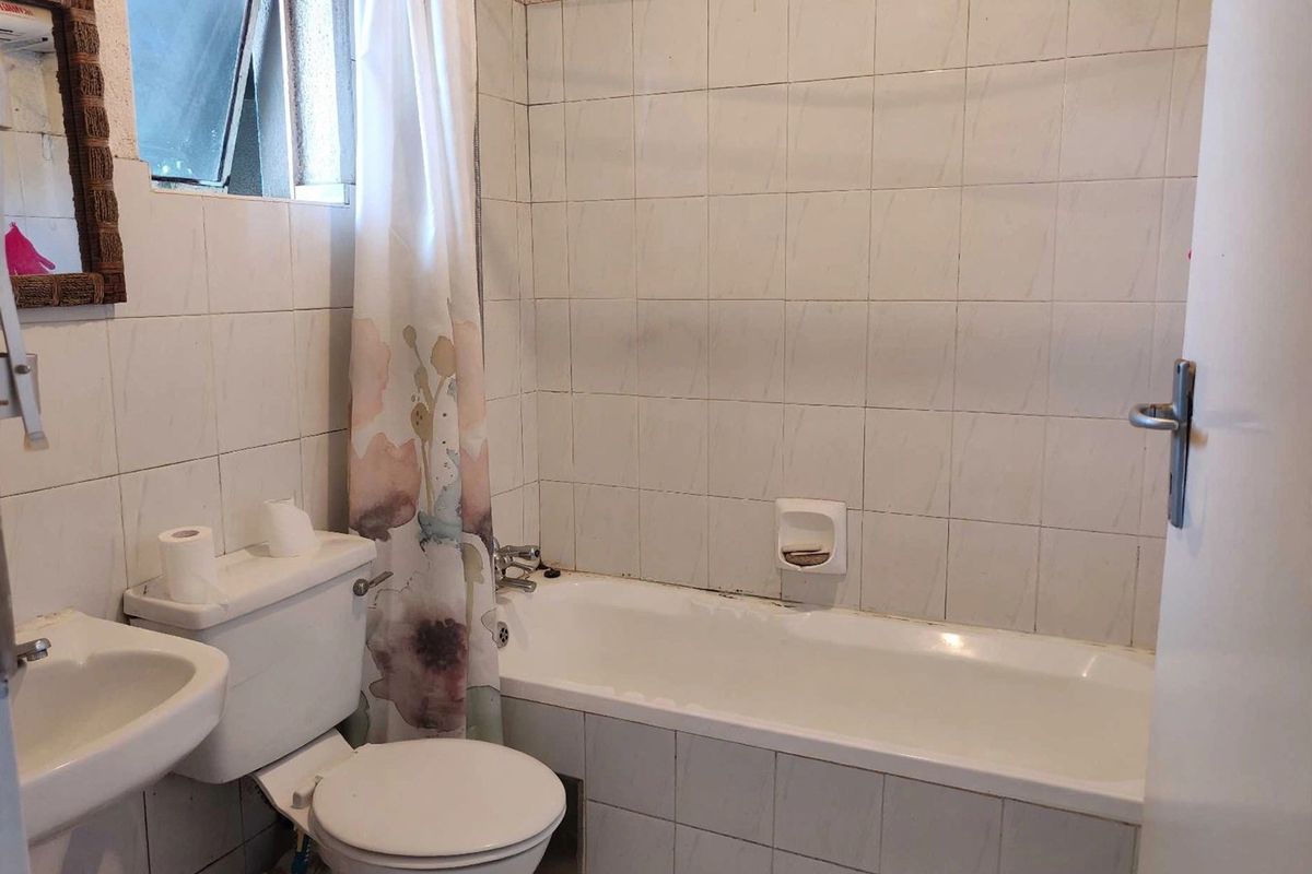 A dated bathroom featuring a standard bathtub, pedestal sink, and toilet with full-height wall tiling and an awning window.