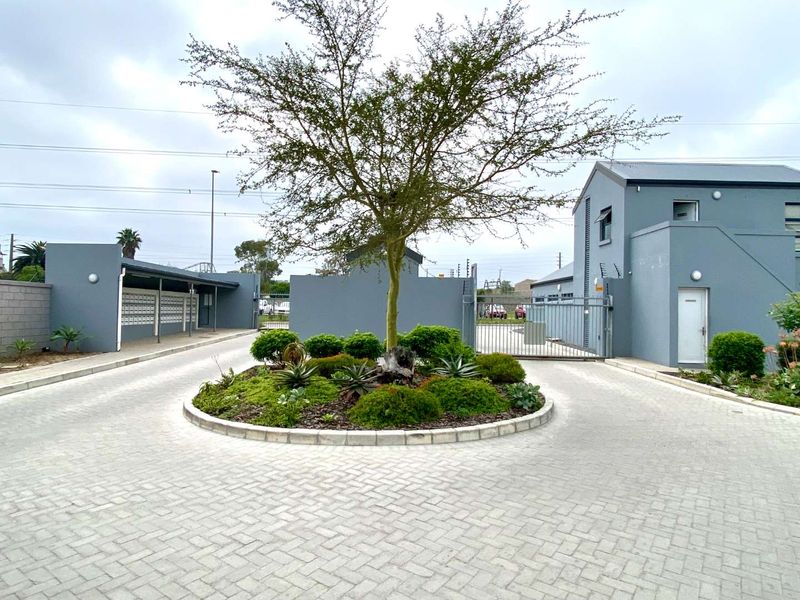 A well-maintained apartment complex entrance featuring a paved driveway, central landscaped roundabout, and secure gated access.