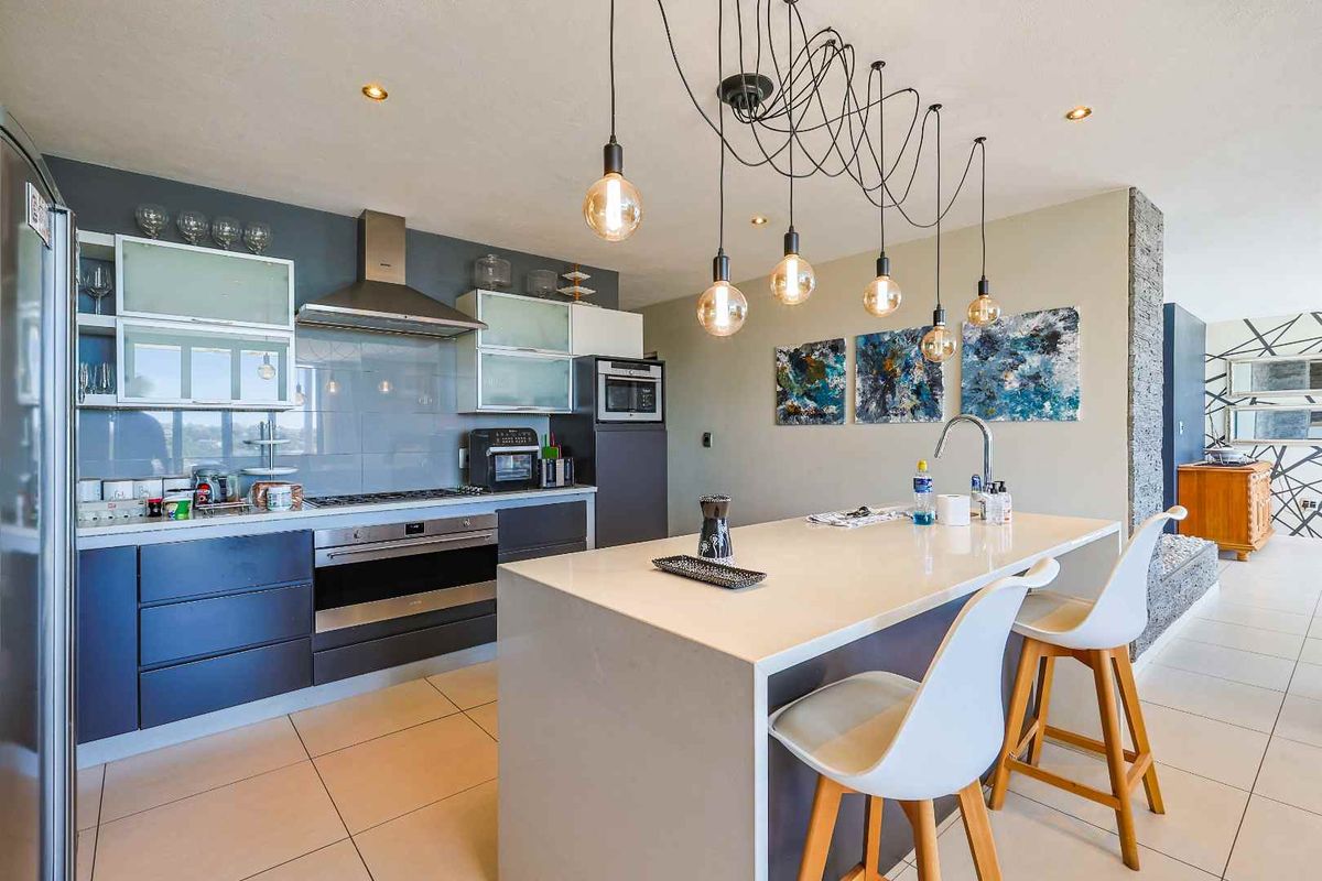 Modern kitchen featuring a central island with breakfast bar, sleek cabinetry, stainless steel extractor fan, built-in oven, and tiled flooring.