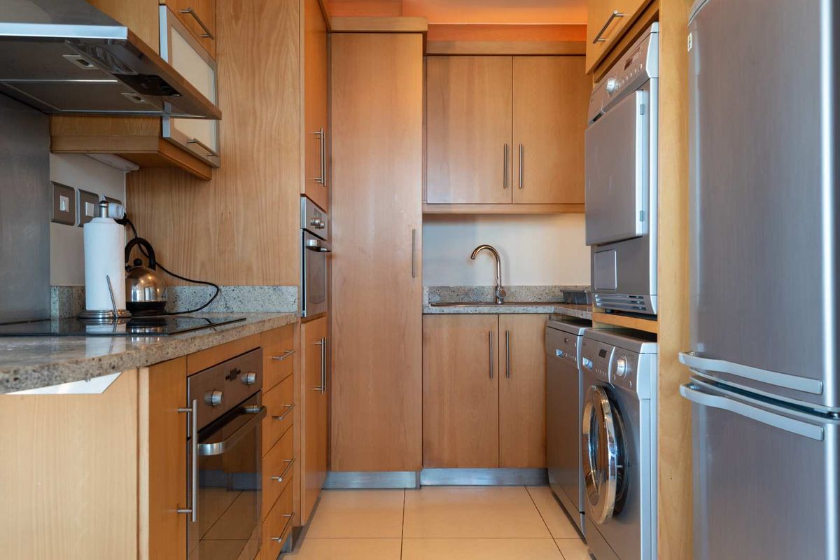 Compact kitchen featuring light wood cabinetry, granite countertops, integrated oven, hob, extractor fan, and dedicated space for laundry appliances.