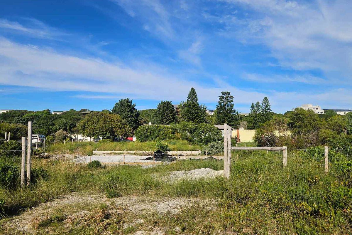 A vacant residential plot featuring a concrete foundation slab and perimeter wire fencing, surrounded by established coastal vegetation.