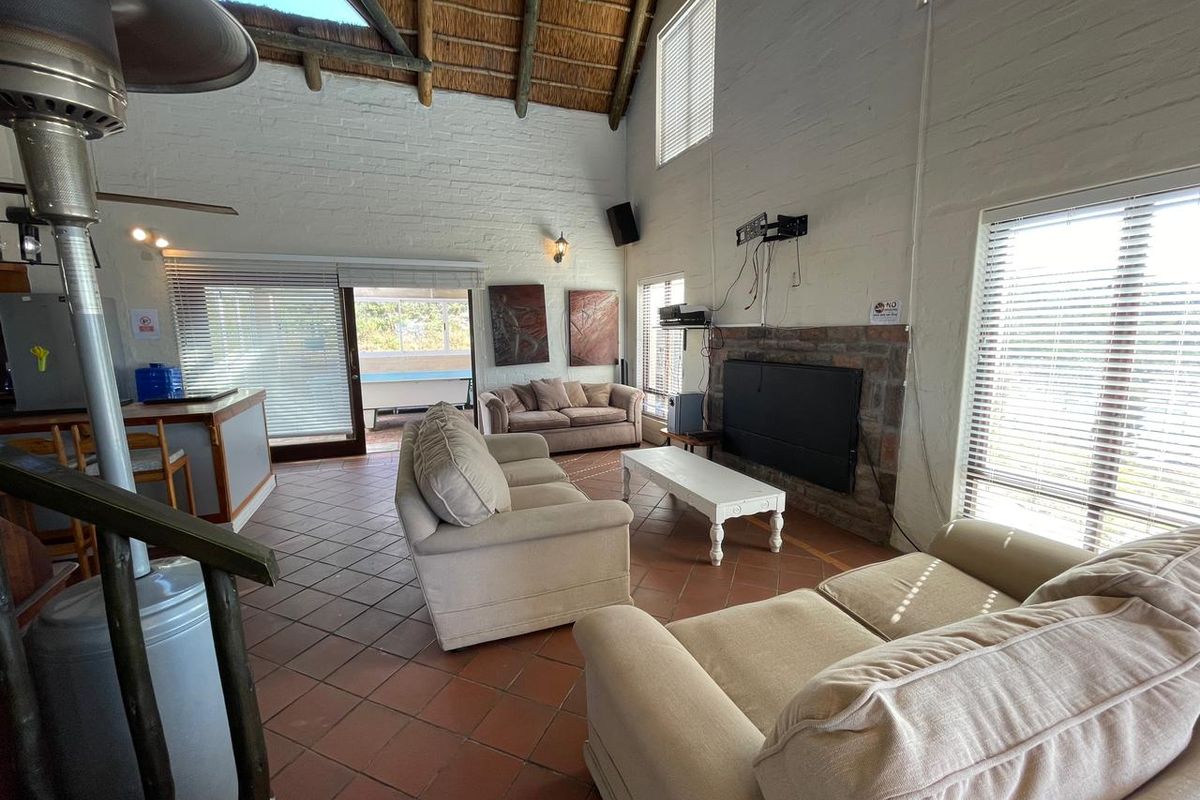 Spacious living area featuring a high vaulted thatched ceiling, exposed brick fireplace, tiled flooring, and large windows providing ample natural light.