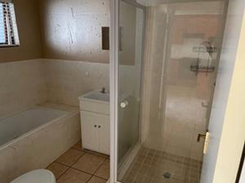 A functional bathroom featuring a built-in bathtub, separate shower enclosure, and a vanity cabinet with tiled flooring and wall finishes.