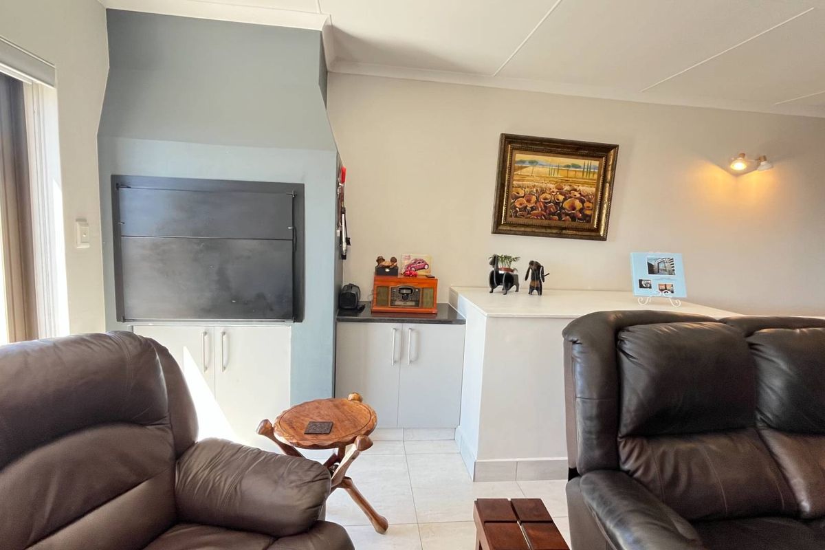 Living area featuring a built-in indoor braai fireplace and custom cabinetry, finished with tiled flooring and neutral wall tones.