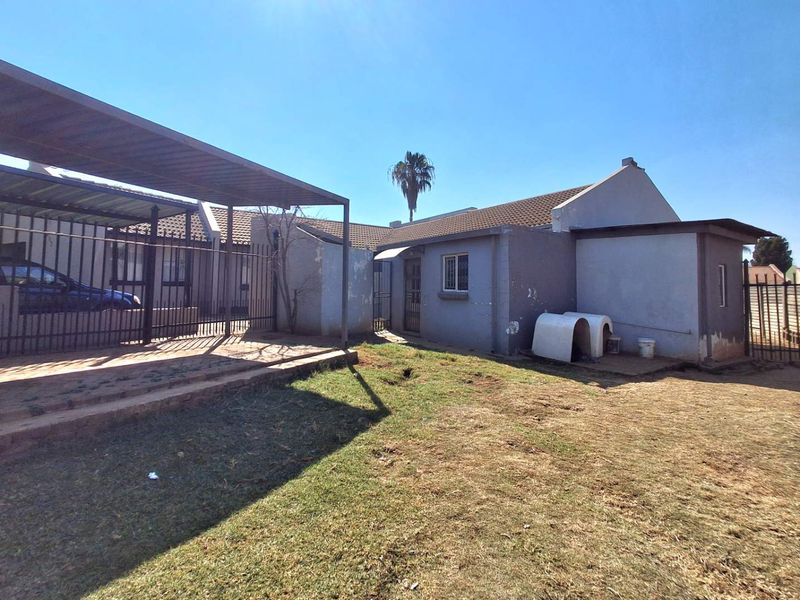 Rear exterior view of the property featuring a paved patio, metal carport structure, and a fenced garden area with a tiled roof.