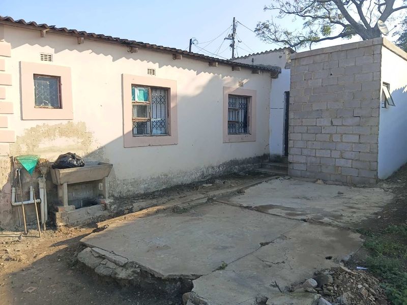 Rear exterior view of the property featuring a concrete patio area, external utility sink, and unfinished brickwork sections requiring maintenance.