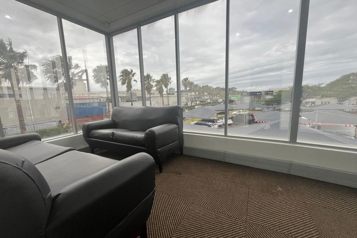 A bright office space featuring extensive floor-to-ceiling windows providing natural light and exterior views, finished with carpeted flooring and a suspended ceiling.