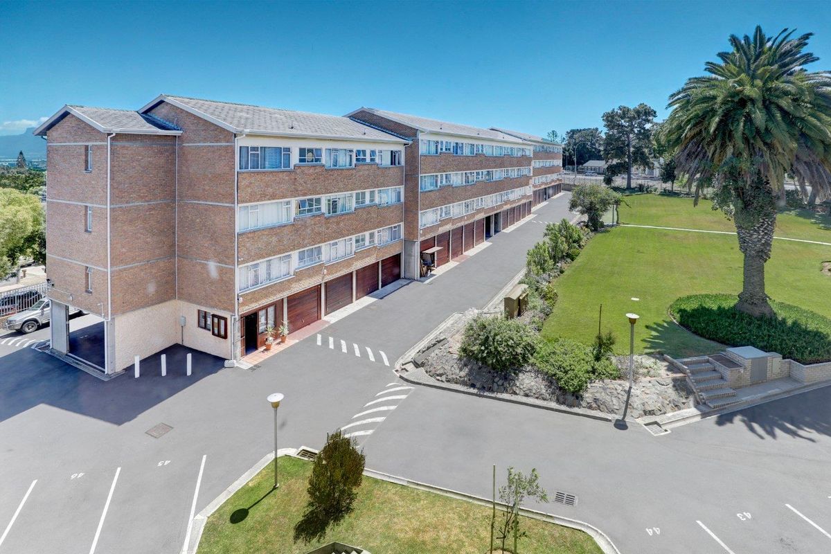Aerial view of the apartment complex featuring brick facade, multiple garage units, paved driveway, and landscaped communal garden areas.