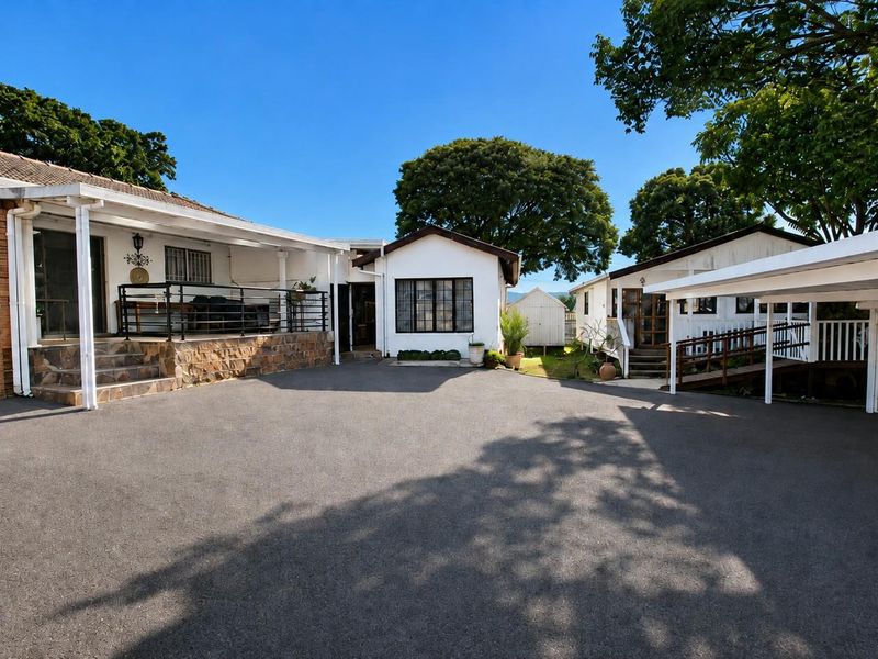 Spacious paved driveway area featuring a covered patio, carport, and accessible timber ramp leading to the main residence and secondary structure.