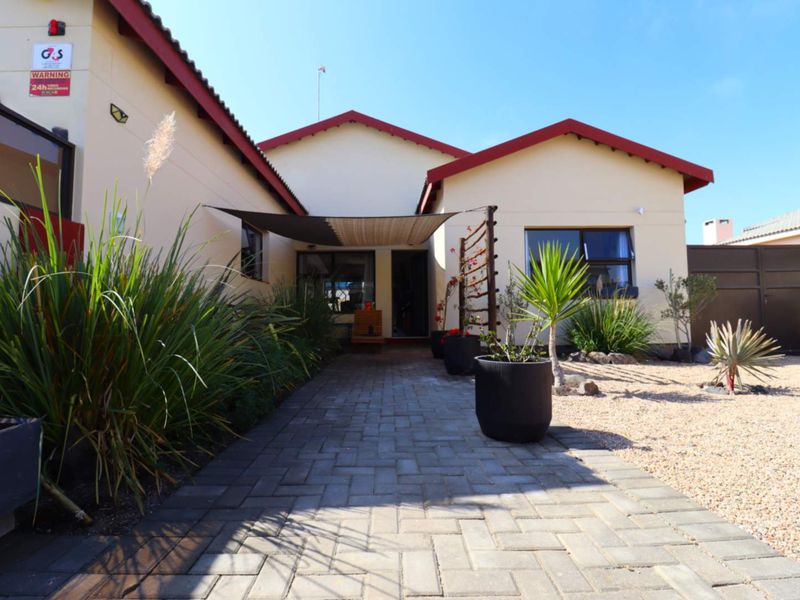 Front exterior view of the house featuring a paved walkway, shade sail, and low-maintenance landscaped garden area.
