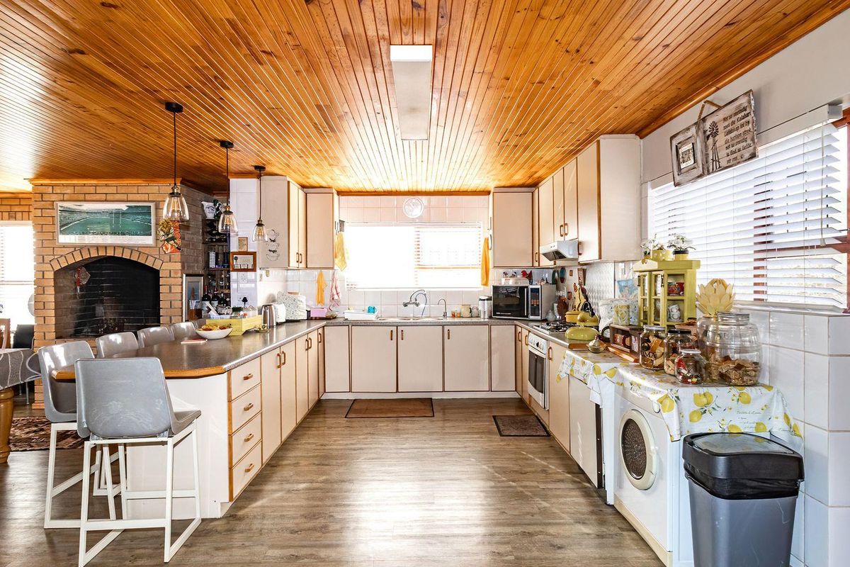 Spacious kitchen featuring a distinctive timber-clad ceiling, brick fireplace, and functional cabinetry layout with integrated appliances and ample counter space.