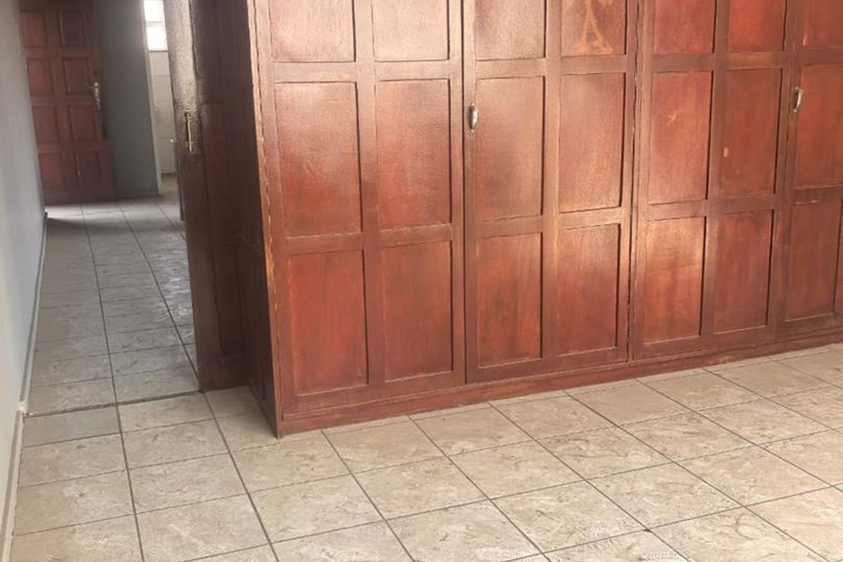 A bedroom featuring extensive built-in wooden cabinetry and tiled flooring, with a doorway leading to an adjacent room.
