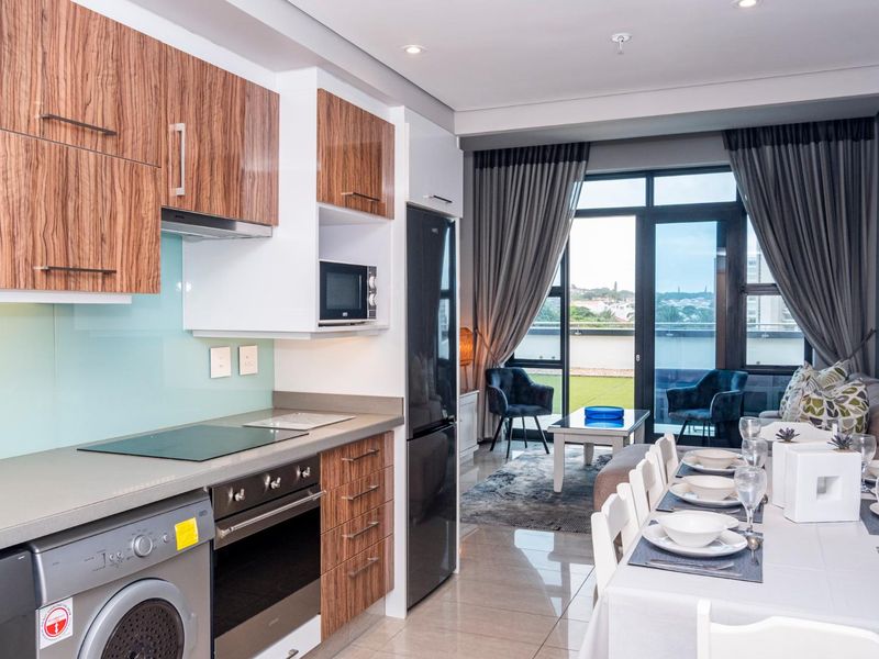 Modern open-plan apartment featuring a sleek kitchen with integrated appliances, flowing into a dining area and living space with access to a private balcony.