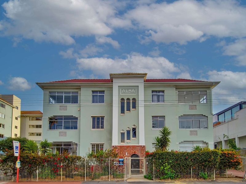 Front elevation of Alma Court apartment building featuring a symmetrical facade, tiled roof, and secure perimeter fencing with a pedestrian entrance.