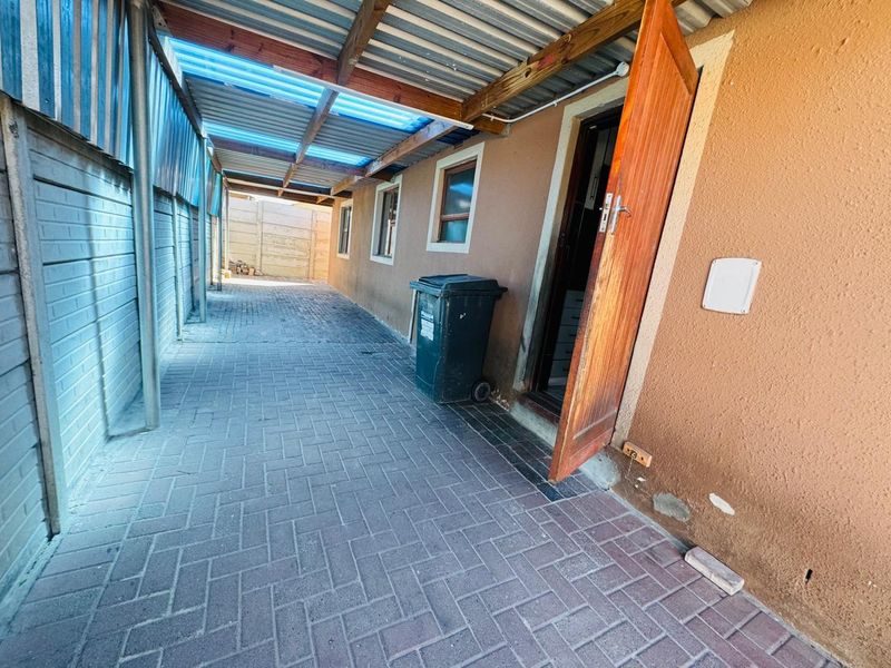 A narrow, paved side passage featuring a covered walkway with a timber structure and corrugated roofing, providing access to the rear of the townhouse.