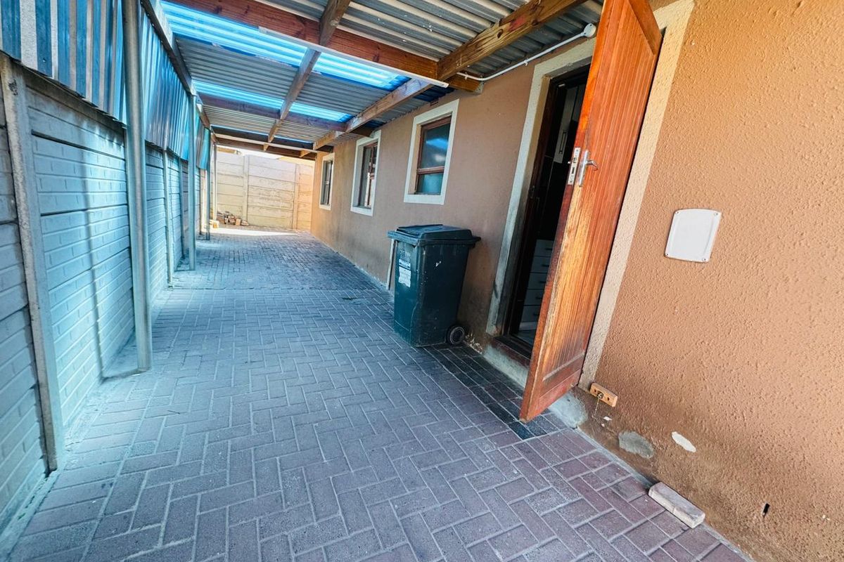 A narrow, paved side passage featuring a covered walkway with a timber structure and corrugated roofing, providing access to the rear of the townhouse.
