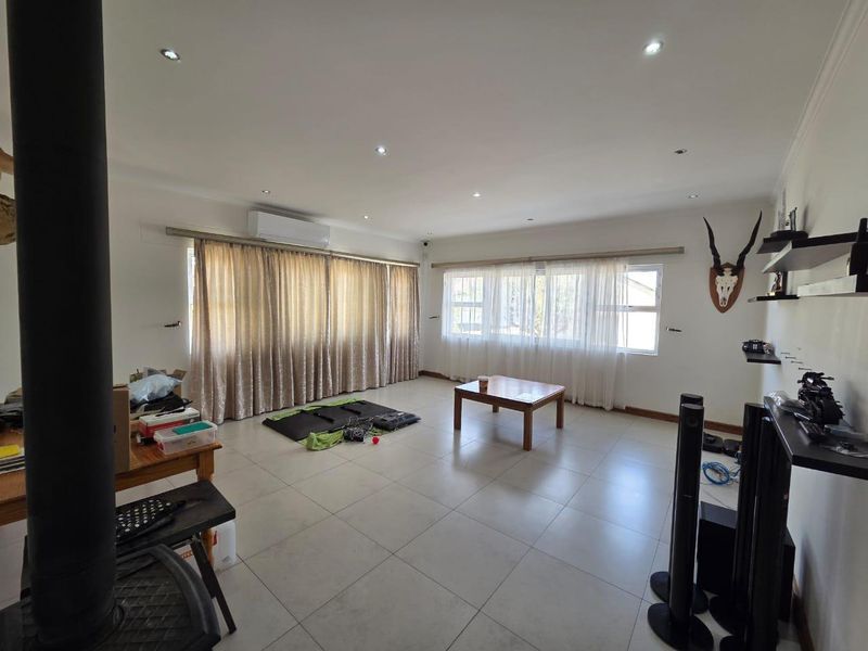 Spacious living room featuring large windows with curtain tracks, tiled flooring, a wood-burning fireplace, and a wall-mounted split-system air conditioner.