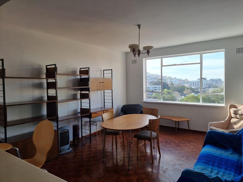 A bright living area featuring original parquet flooring, large windows with city views, and a classic ceiling light fixture.