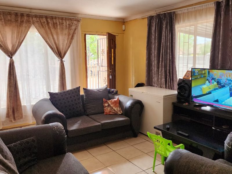 A functional living room featuring tiled flooring and direct access to the exterior through a sliding door with a security gate.