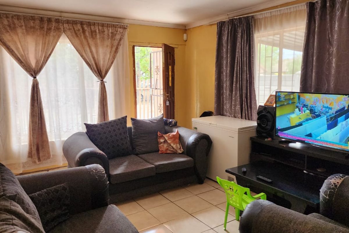 A functional living room featuring tiled flooring and direct access to the exterior through a sliding door with a security gate.