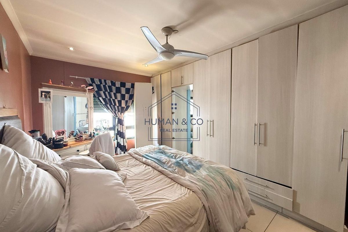 A bedroom featuring extensive built-in floor-to-ceiling wardrobes with light wood-grain finish and a ceiling fan.