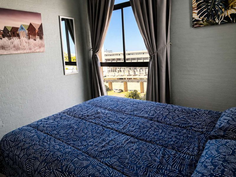 A well-lit bedroom featuring painted brick walls and a large window with views of the surrounding urban area.