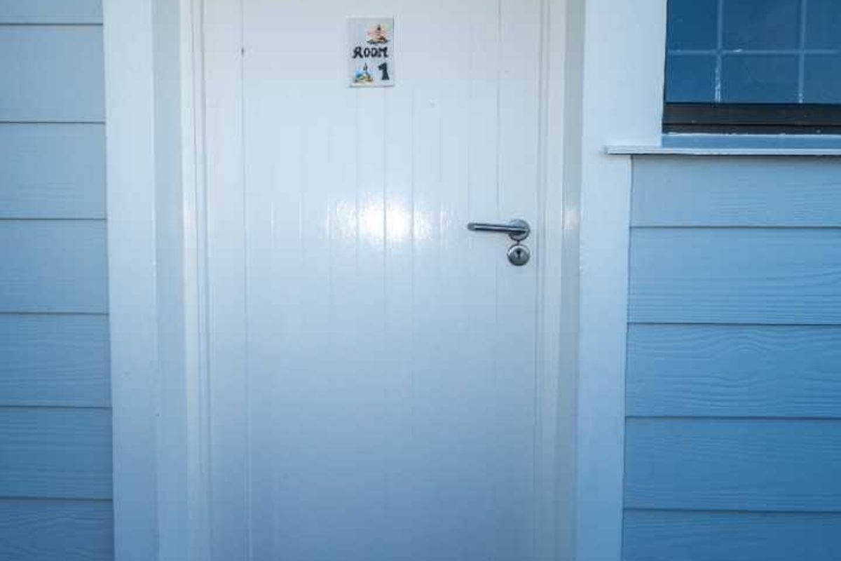 Exterior view of a guest house room entrance featuring timber cladding, a tiled step, and a secure window.
