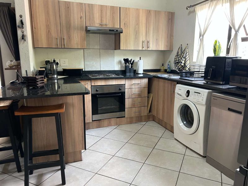 A functional kitchen featuring wood-look cabinetry, granite countertops, integrated appliances, and tiled flooring, providing a practical workspace for daily cooking and laundry needs.