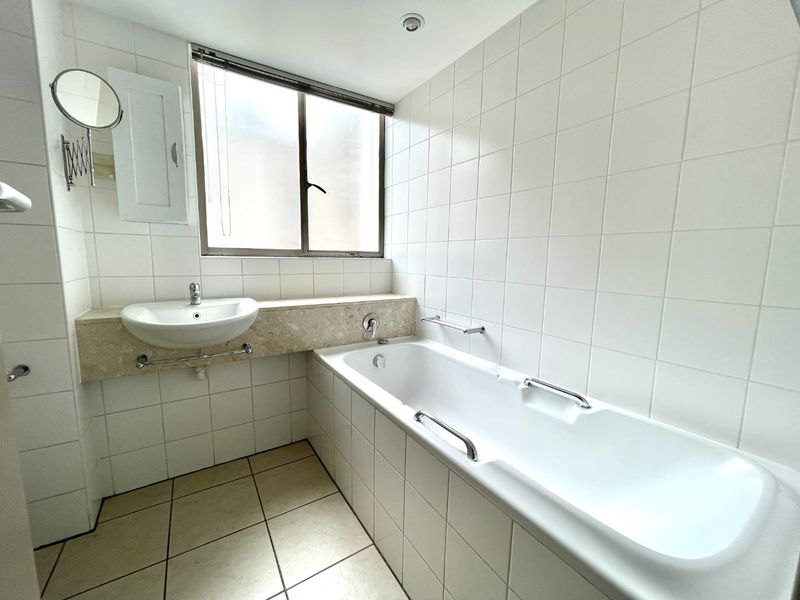 A clean, functional bathroom featuring a built-in bathtub, wall-mounted basin with stone vanity top, and neutral white wall tiling.