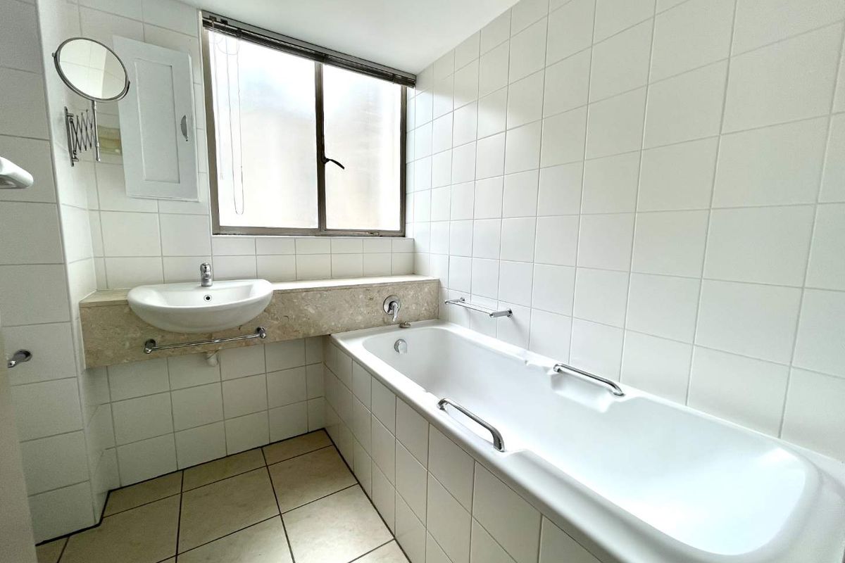 A clean, functional bathroom featuring a built-in bathtub, wall-mounted basin with stone vanity top, and neutral white wall tiling.
