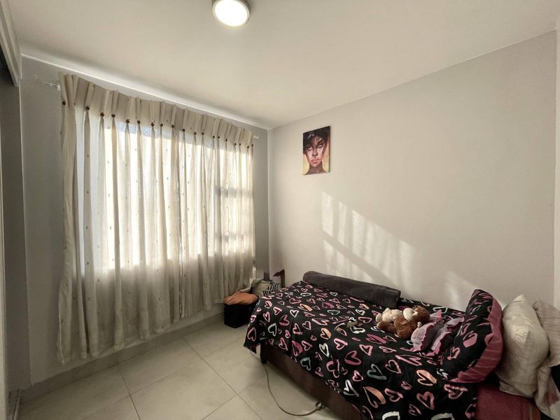 A functional bedroom featuring neutral wall finishes, tiled flooring, and a large window with installed curtain tracks.