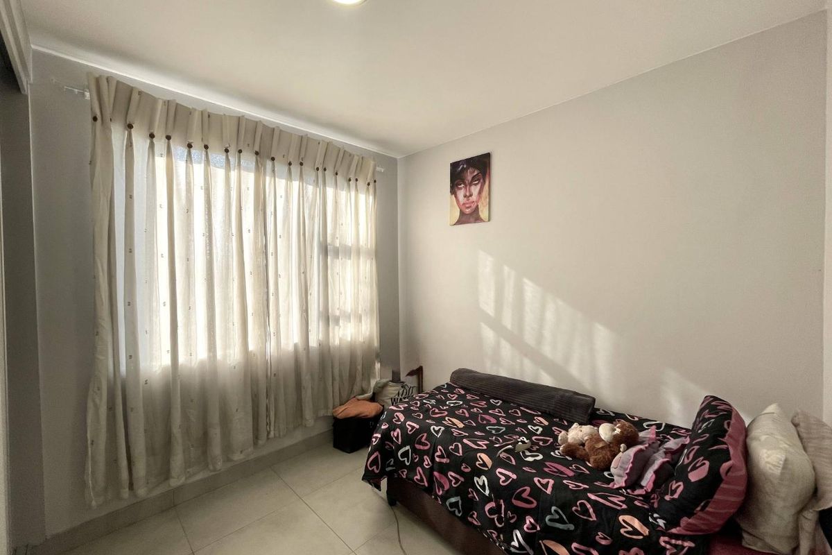 A functional bedroom featuring neutral wall finishes, tiled flooring, and a large window with installed curtain tracks.