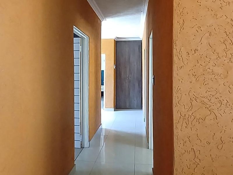 A bright hallway featuring tiled flooring, textured wall finishes, and a built-in cupboard, providing access to adjacent rooms.
