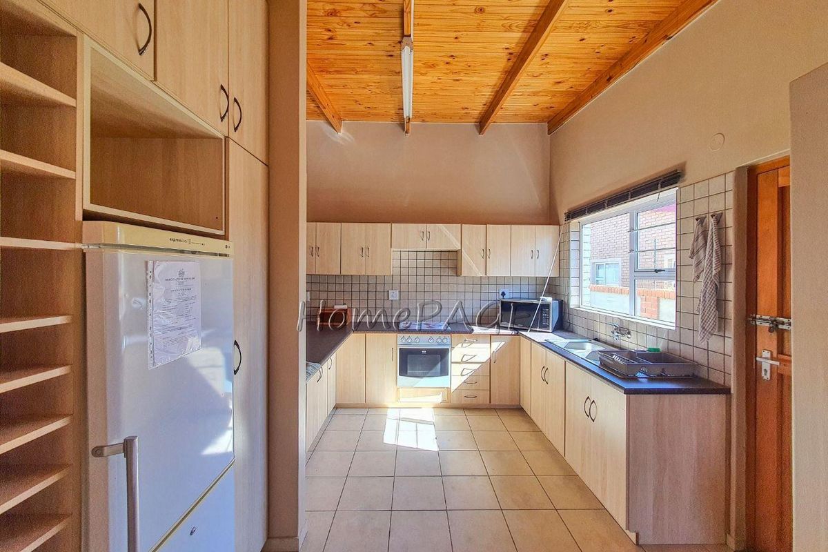 A functional kitchen featuring light wood cabinetry, tiled flooring, a built-in oven and hob, and a high exposed timber beam ceiling.