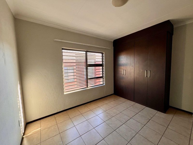 A clean, empty bedroom featuring tiled flooring and dark wood built-in cupboards, providing a neutral space ready for personalization.
