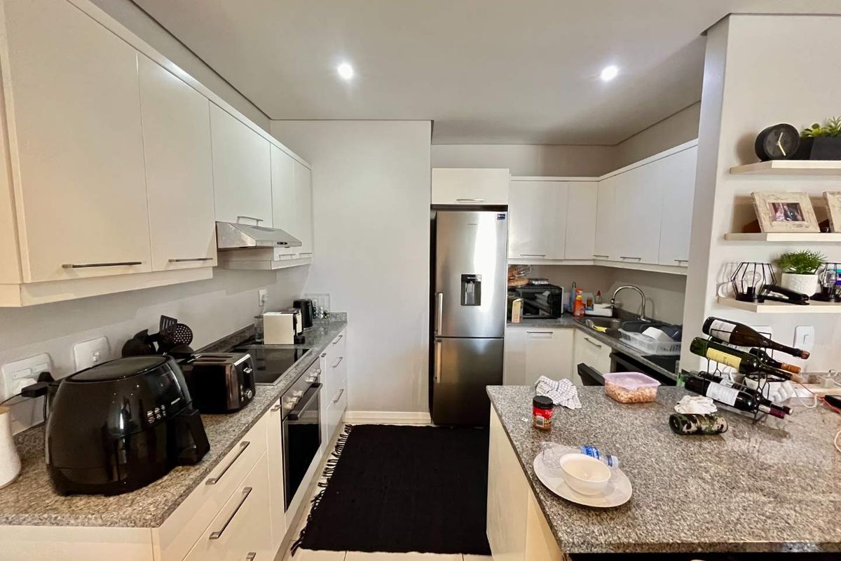 Modern kitchen featuring white cabinetry, granite countertops, built-in oven, hob, extractor fan, and a breakfast bar island.