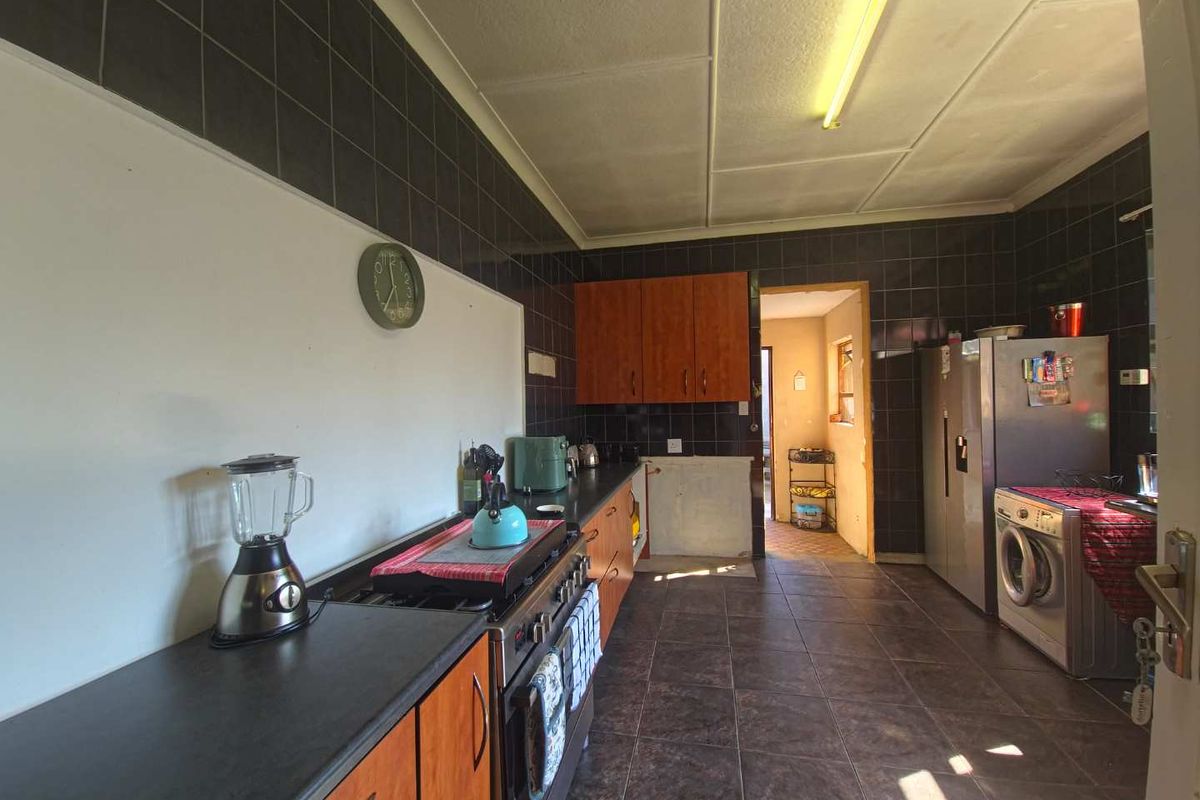 A functional kitchen featuring dark tiled walls, wooden cabinetry, a gas stove, and tiled flooring, with an adjacent doorway leading to another area.