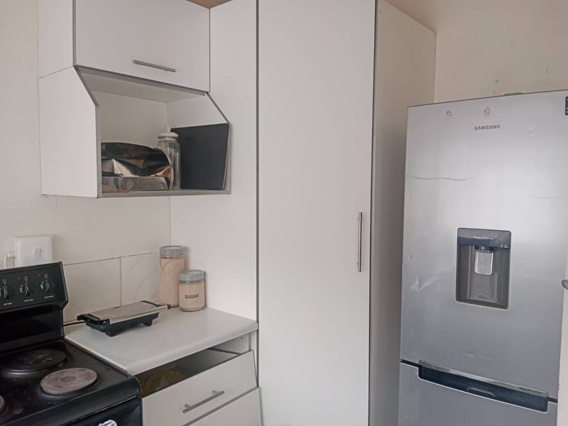 A compact kitchen area featuring white built-in cabinetry, a laminate countertop, and an integrated stove, offering functional storage and preparation space.