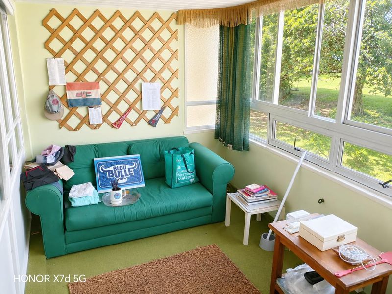 A sunroom or enclosed balcony featuring large windows with garden views and a decorative timber lattice wall panel.