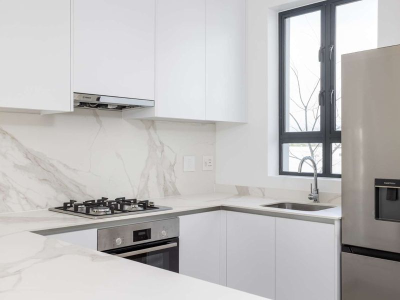 Modern kitchen featuring white cabinetry, marble-look stone countertops and backsplash, integrated gas hob, oven, and stainless steel sink with a sleek finish.