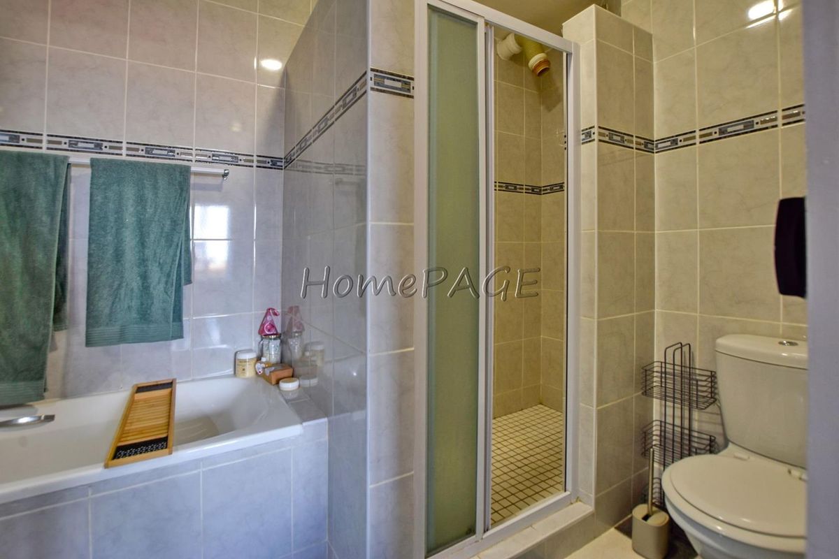 A functional bathroom featuring a built-in bathtub, a separate glass-enclosed shower, and a standard toilet with neutral wall tiling.
